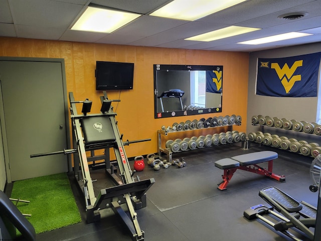 workout area featuring a drop ceiling and wooden walls