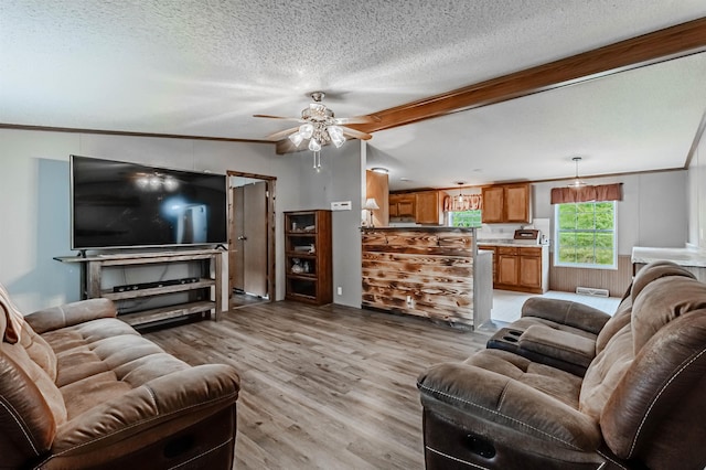 living room featuring ornamental molding, beam ceiling, ceiling fan, light wood-type flooring, and a textured ceiling