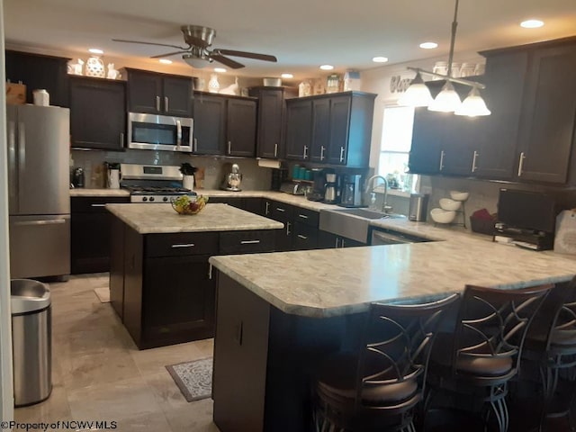 kitchen featuring kitchen peninsula, backsplash, appliances with stainless steel finishes, a kitchen bar, and decorative light fixtures