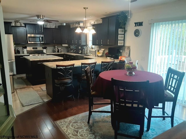 kitchen featuring appliances with stainless steel finishes, a kitchen island, kitchen peninsula, hanging light fixtures, and light hardwood / wood-style flooring