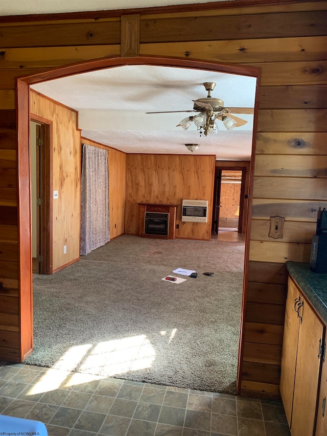 unfurnished living room featuring dark carpet, ceiling fan, heating unit, and wood walls