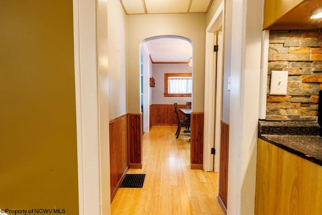 corridor with light hardwood / wood-style flooring, ornamental molding, and wooden walls