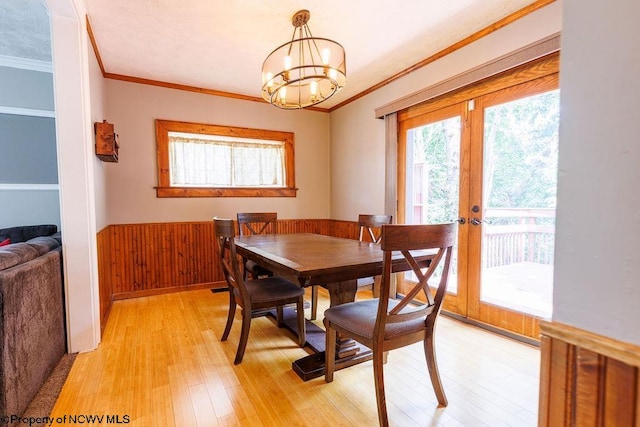 dining room with an inviting chandelier, light hardwood / wood-style flooring, ornamental molding, wood walls, and french doors