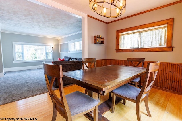 dining area featuring ornamental molding, light hardwood / wood-style flooring, wooden walls, and an inviting chandelier