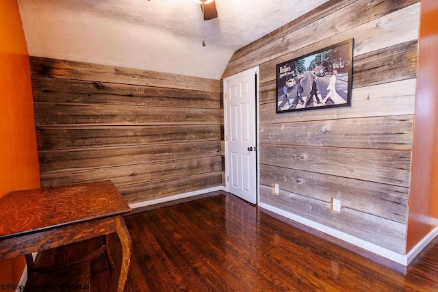 unfurnished room featuring ceiling fan, wood walls, lofted ceiling, and dark hardwood / wood-style flooring