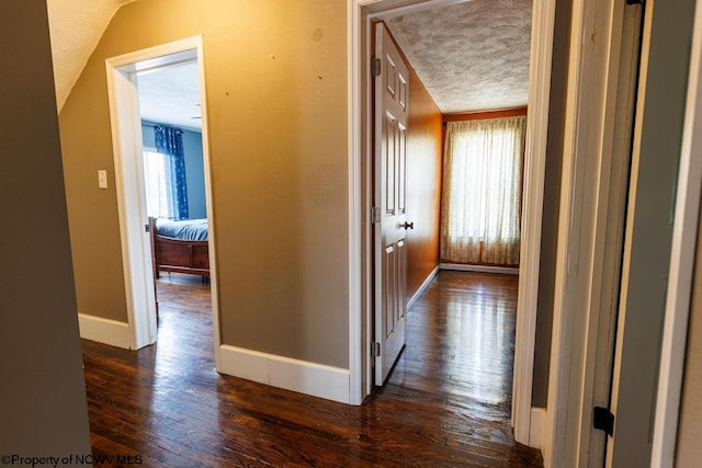 corridor with a wealth of natural light, dark wood-type flooring, and a textured ceiling