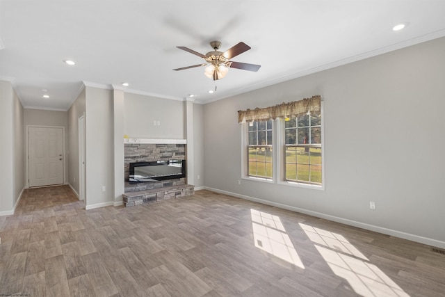 unfurnished living room with crown molding, a stone fireplace, light wood-type flooring, and ceiling fan