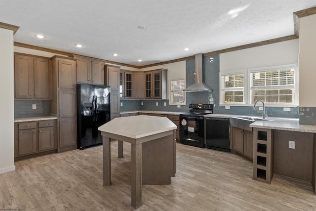 kitchen featuring tasteful backsplash, wall chimney range hood, black appliances, sink, and light hardwood / wood-style flooring