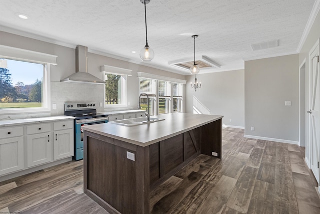 kitchen featuring wall chimney range hood, a healthy amount of sunlight, an island with sink, electric stove, and sink