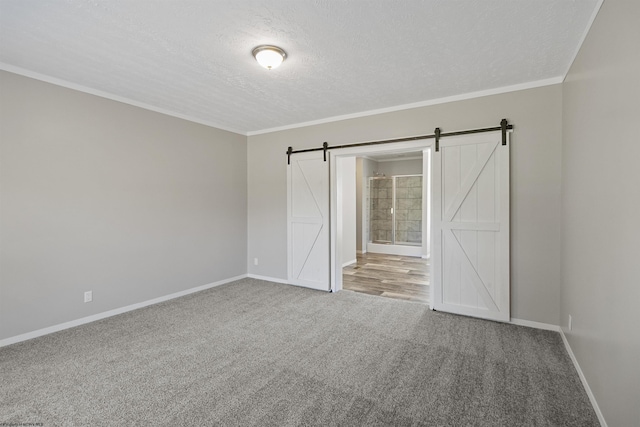 empty room with crown molding, a textured ceiling, a barn door, and carpet flooring