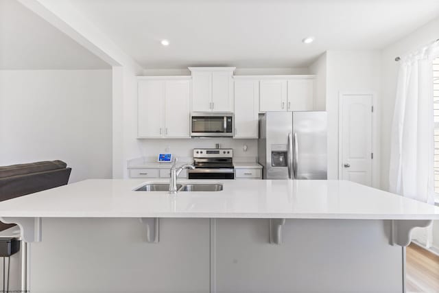 kitchen with a large island with sink, a kitchen breakfast bar, white cabinetry, sink, and stainless steel appliances