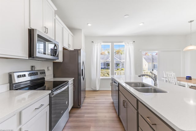 kitchen with white cabinets, sink, light hardwood / wood-style floors, decorative light fixtures, and stainless steel appliances