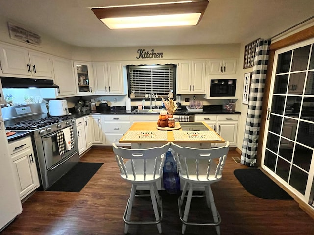 kitchen with dark wood-type flooring, white cabinets, stainless steel gas stove, a kitchen island, and a breakfast bar area