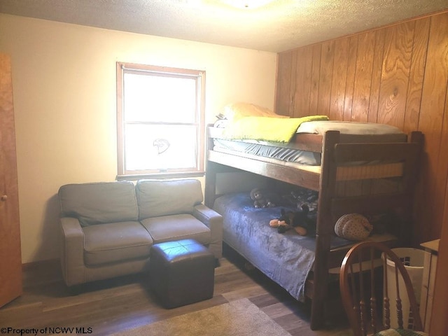 bedroom with wood walls, a textured ceiling, and dark wood-type flooring