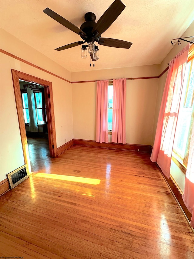 empty room with ceiling fan, a textured ceiling, light hardwood / wood-style floors, and plenty of natural light