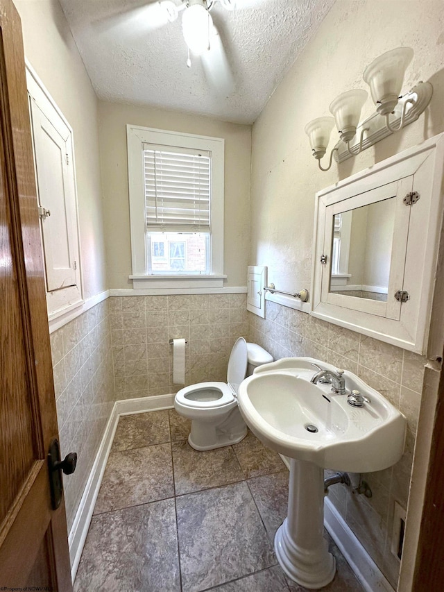 bathroom with ceiling fan, a textured ceiling, tile walls, toilet, and tile patterned flooring