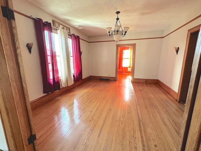 spare room featuring an inviting chandelier, light hardwood / wood-style flooring, a textured ceiling, and a wealth of natural light