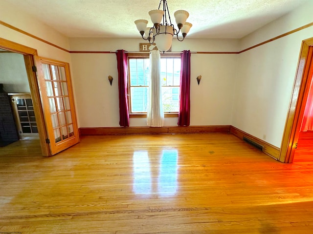 unfurnished room with light hardwood / wood-style flooring, a textured ceiling, and a notable chandelier