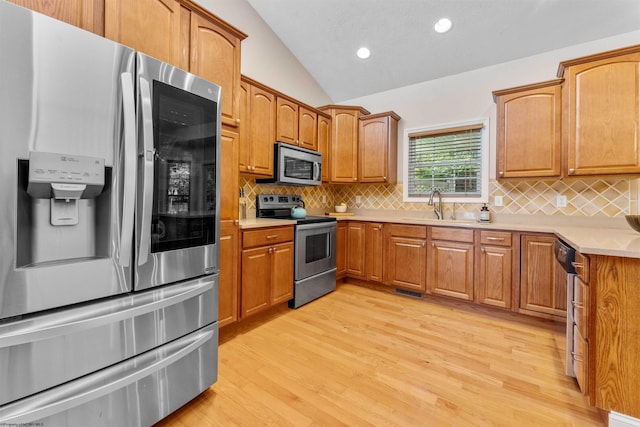 kitchen with backsplash, light wood-type flooring, vaulted ceiling, sink, and stainless steel appliances