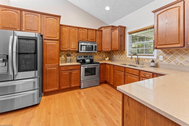 kitchen with appliances with stainless steel finishes, sink, light wood-type flooring, backsplash, and vaulted ceiling