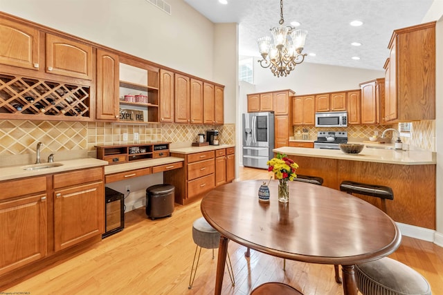 kitchen with decorative backsplash, light wood-type flooring, pendant lighting, a notable chandelier, and stainless steel appliances