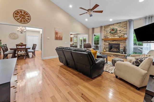 living room with a wealth of natural light, light hardwood / wood-style floors, a stone fireplace, and high vaulted ceiling