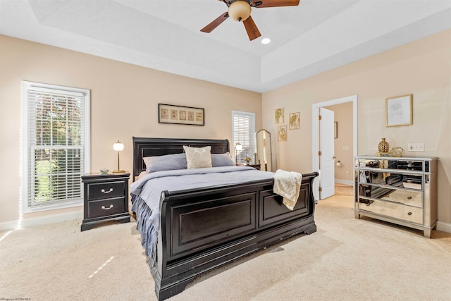 bedroom featuring light colored carpet, a raised ceiling, and ceiling fan