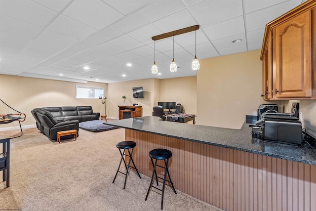 kitchen with a breakfast bar area, light carpet, kitchen peninsula, a drop ceiling, and decorative light fixtures