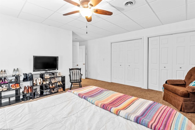 bedroom with a drop ceiling, two closets, carpet flooring, and ceiling fan