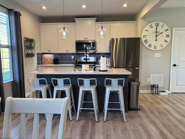 kitchen with tasteful backsplash, white cabinetry, a kitchen island with sink, light hardwood / wood-style flooring, and stainless steel appliances