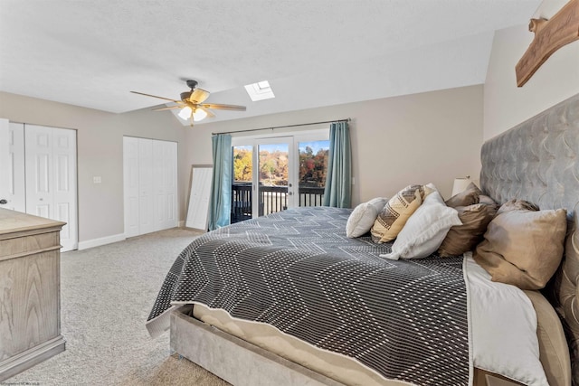bedroom featuring light colored carpet, ceiling fan, access to exterior, multiple closets, and a skylight