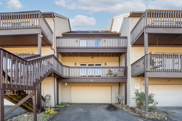 rear view of house featuring aphalt driveway, a balcony, stairs, and an attached garage
