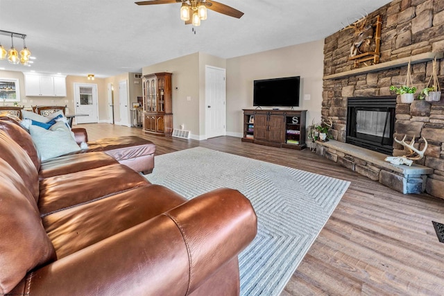 living area featuring visible vents, baseboards, a fireplace, wood finished floors, and ceiling fan with notable chandelier