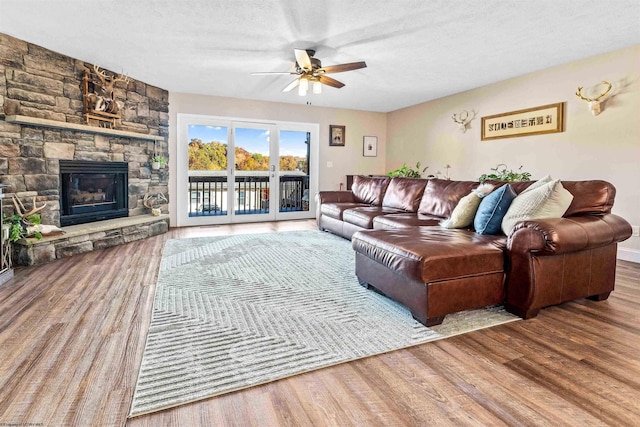 living area featuring ceiling fan, a stone fireplace, and wood finished floors