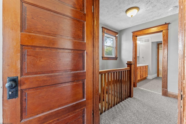 corridor with light carpet and a textured ceiling