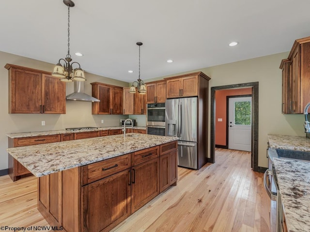 kitchen with light hardwood / wood-style floors, stainless steel appliances, pendant lighting, and an island with sink