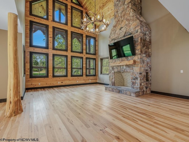 unfurnished living room featuring light hardwood / wood-style flooring, high vaulted ceiling, an inviting chandelier, and a stone fireplace