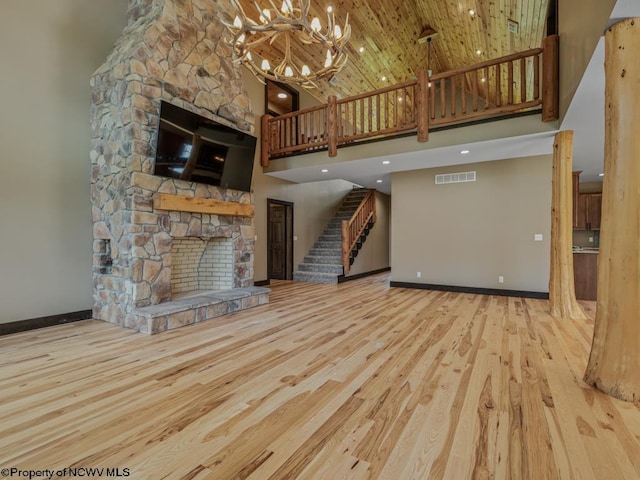 unfurnished living room with a towering ceiling, a stone fireplace, and light hardwood / wood-style floors