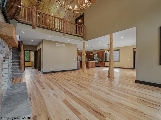 unfurnished living room with plenty of natural light, a high ceiling, light wood-type flooring, and an inviting chandelier