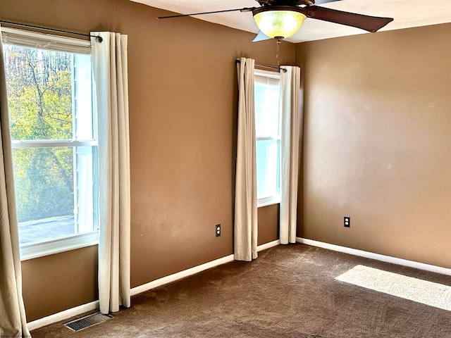 empty room featuring dark carpet, plenty of natural light, and ceiling fan