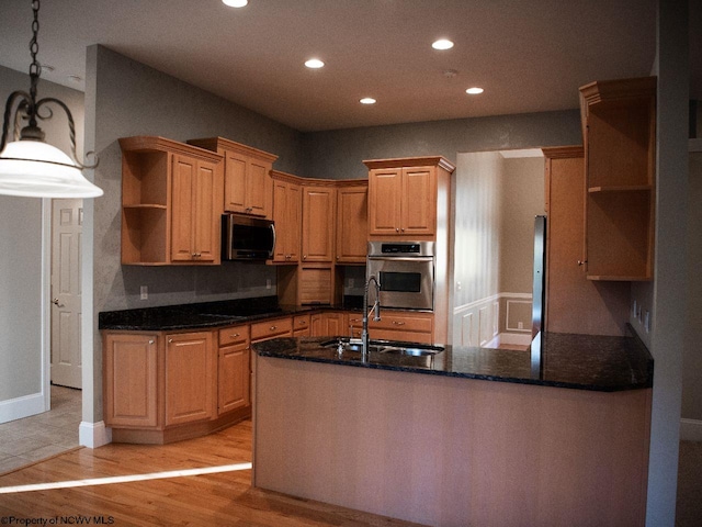 kitchen featuring appliances with stainless steel finishes, sink, kitchen peninsula, hanging light fixtures, and light hardwood / wood-style floors