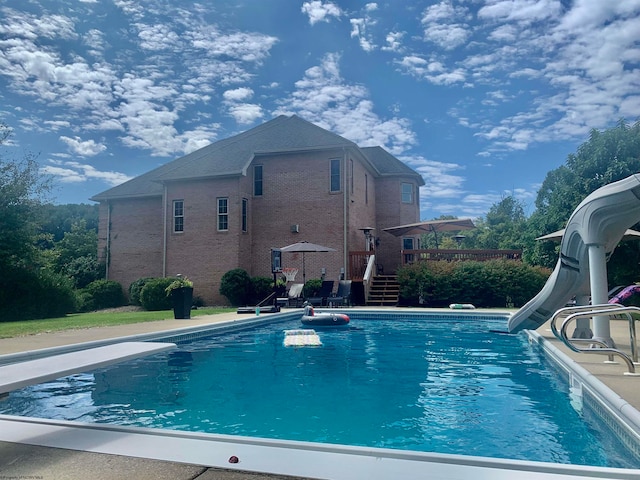 view of swimming pool with a wooden deck, a water slide, and a diving board