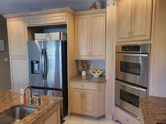 kitchen with stone counters, sink, light tile patterned flooring, stainless steel appliances, and light brown cabinets