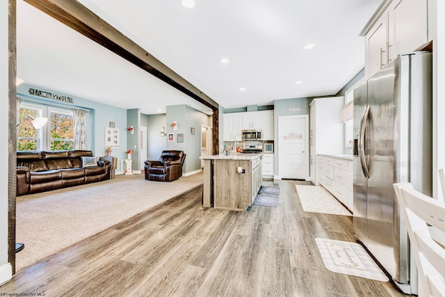 kitchen featuring white cabinets, backsplash, appliances with stainless steel finishes, light wood-type flooring, and a center island