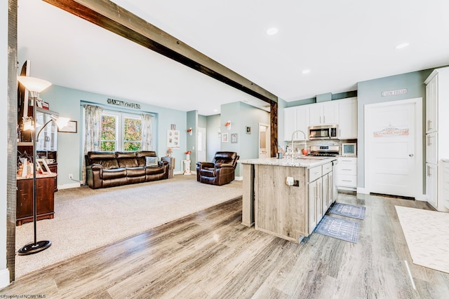 kitchen with a kitchen island with sink, beamed ceiling, light hardwood / wood-style flooring, stainless steel appliances, and white cabinets