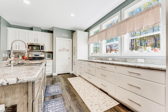 kitchen featuring dark wood-type flooring, light stone countertops, appliances with stainless steel finishes, and white cabinets