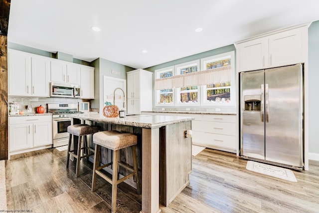 kitchen featuring white cabinets, a kitchen island, appliances with stainless steel finishes, a kitchen breakfast bar, and light wood-type flooring