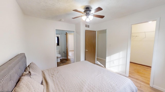 bedroom featuring a walk in closet, ceiling fan, light hardwood / wood-style flooring, a closet, and ensuite bath