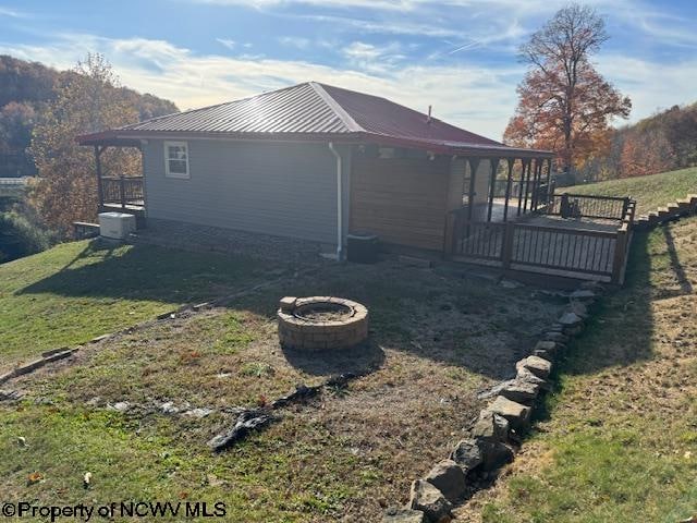 view of property exterior with a wooden deck, an outdoor fire pit, a lawn, and central AC unit