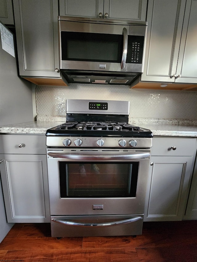 kitchen featuring dark hardwood / wood-style floors, backsplash, gray cabinets, appliances with stainless steel finishes, and light stone counters